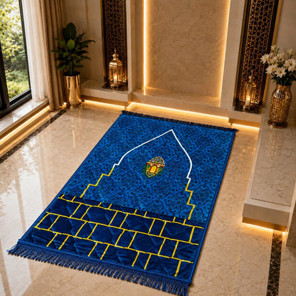A blue patterned prayer rug with gold and white architectural motifs and fringe, displayed on a polished marble floor in a modern interior setting.