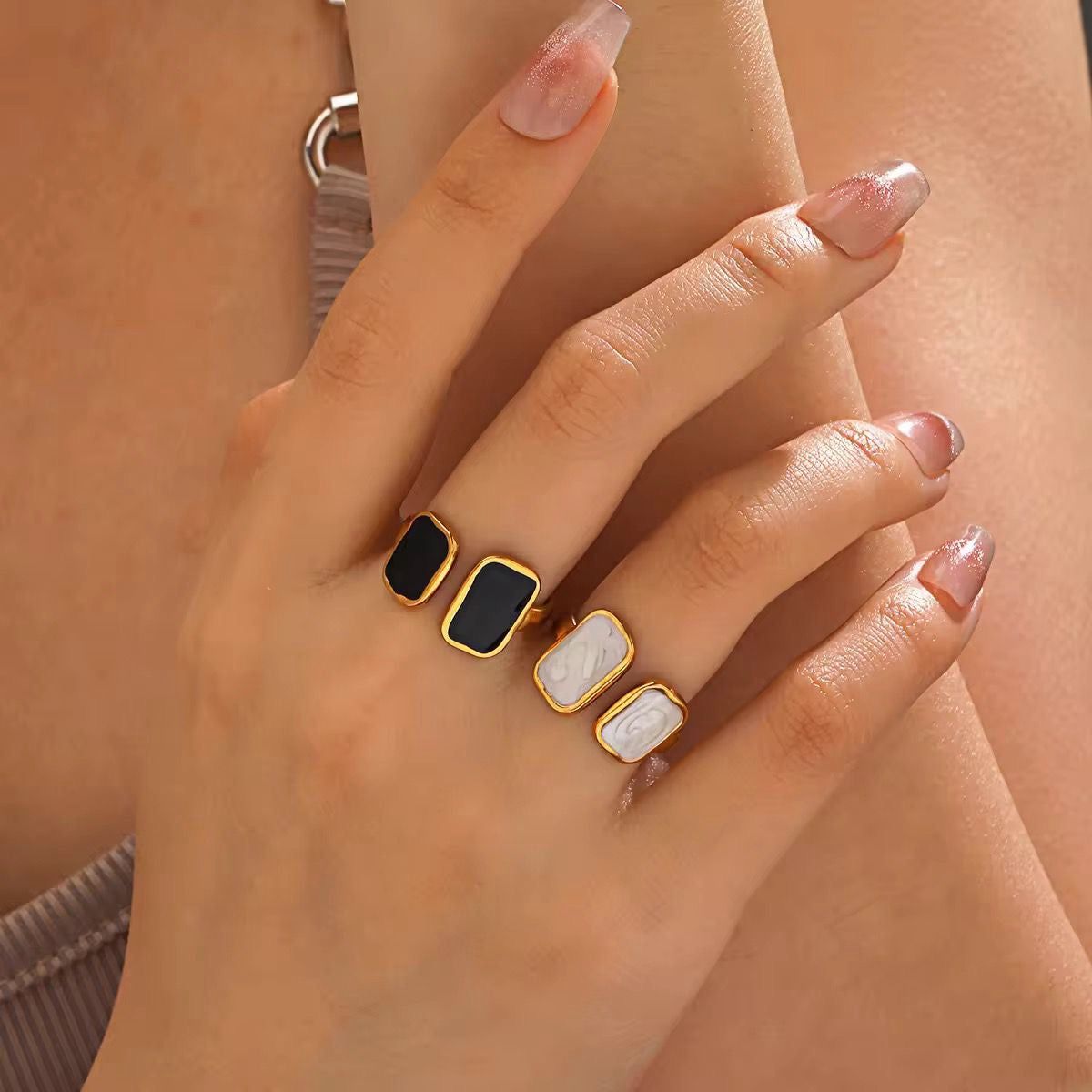 Close-up of a hand wearing two rings with black and gold bands on a neutral background