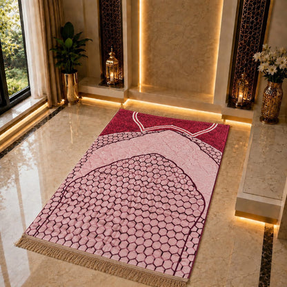 A rectangular prayer rug with a pink and burgundy Islamic arch pattern and beige fringe, displayed on a polished marble floor in a luxurious, warmly lit mosque or prayer hall.