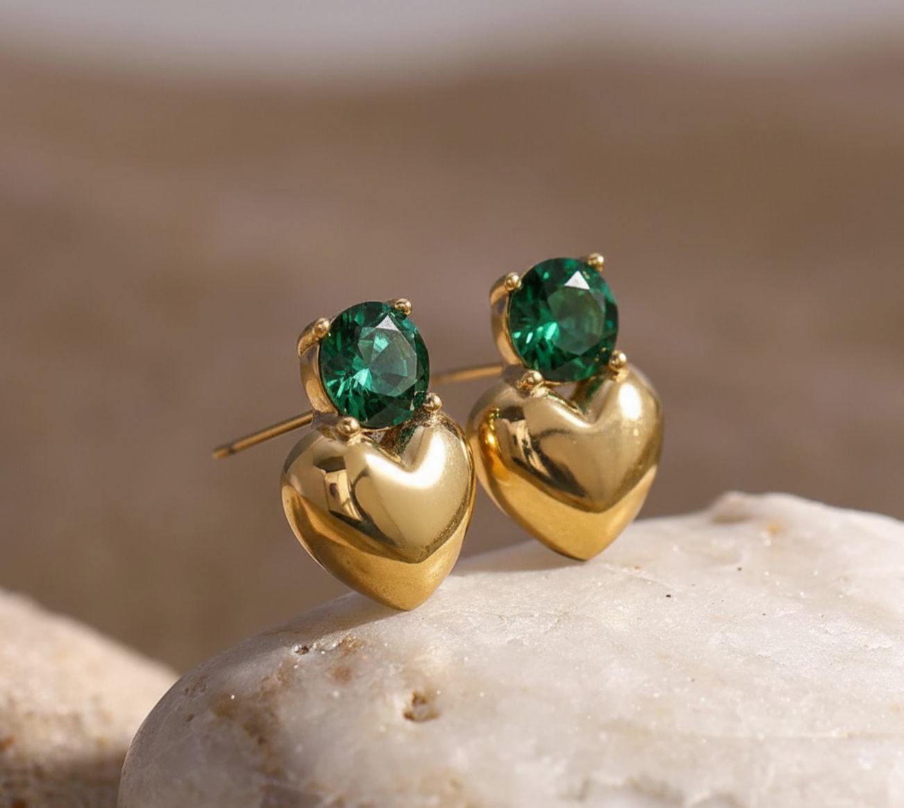 Gold earrings with green gemstones on a stone surface
