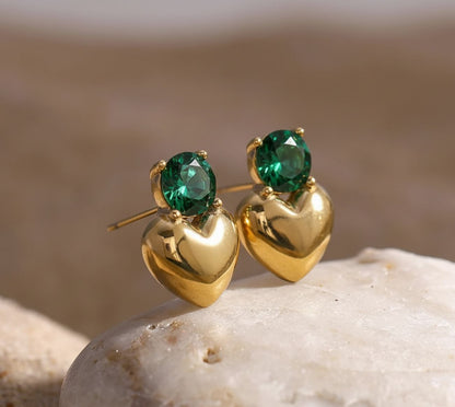 Gold earrings with green gemstones on a stone surface