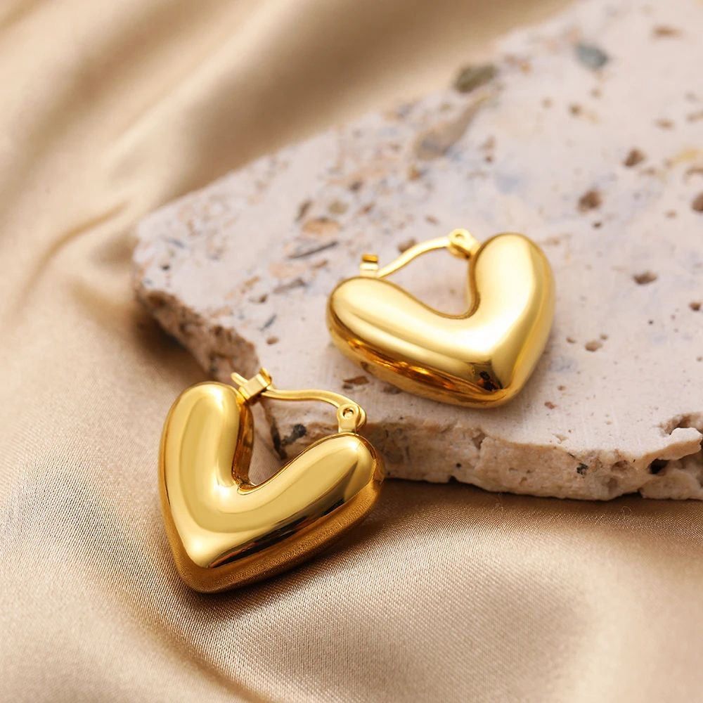 Gold heart-shaped earrings on a textured stone surface with a soft fabric background