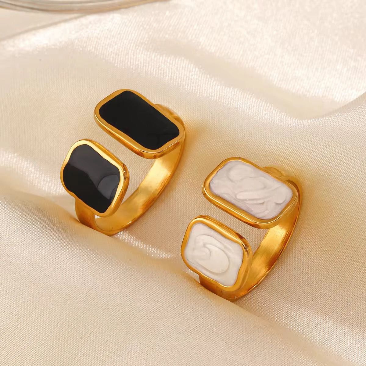 Two gold rings with black and white stone inlays on a beige fabric background