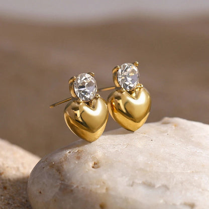 Gold heart-shaped earrings with clear gemstones on a stone surface