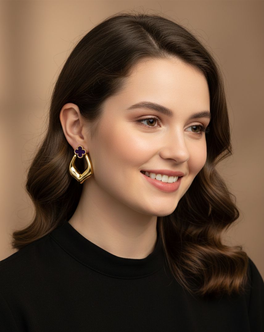 Woman wearing gold earrings with a purple gemstone against a neutral background