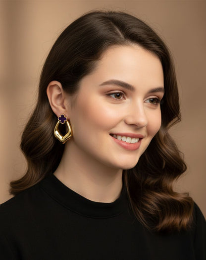 Woman wearing gold earrings with a purple gemstone against a neutral background