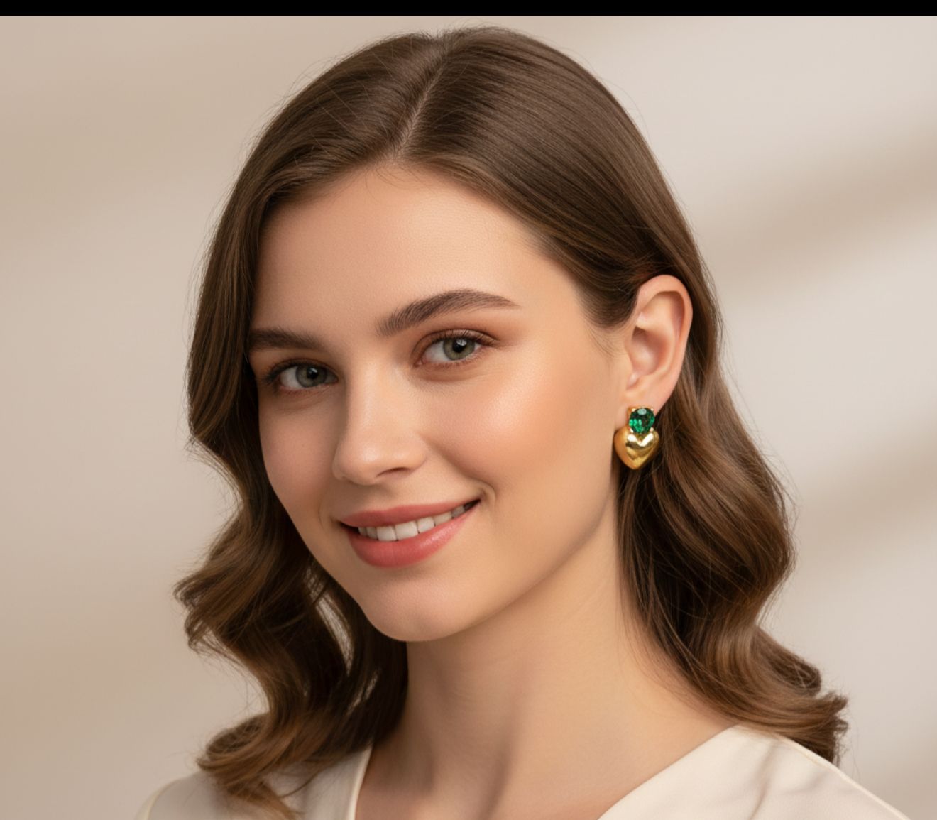 Woman wearing gold earrings with green gemstones against a neutral background